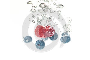 BlueberryÃ¢â¬â¢s and raspberries splashing into crystal clear water with air bubbles and sinking